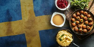 top visie van kottbullar vlees ballen met kommen van saus, aardappel puree en veenbessen Aan de kant met een Zweeds vlag in de achtergrond foto