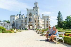 een paar van toeristen zijn zittend Aan een bank in voorkant van de mooi kasteel hluboka nad vltavou - Tsjechisch republiek. foto