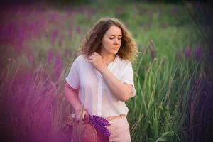 jong vrouw staat in wit overhemd in veld- van Purper en roze lupinen. mooi jong vrouw met gekruld haar- buitenshuis Aan een weide, lupinen bloesem. zonsondergang of zonsopkomst, helder avond licht foto