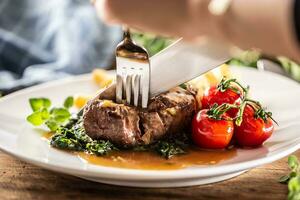 detail van een vork en mes besnoeiing in een sappig perfect gemaakt steak Aan een bord. foto