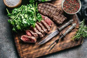 plakjes van sappig gegrild rundvlees steak met vork en mes Aan een slager bord foto