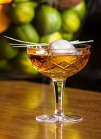 smakelijk alcohol drinken met groot ijs bal binnen. geserveerd in elegant glas met sappig limoenen in de achtergrond foto