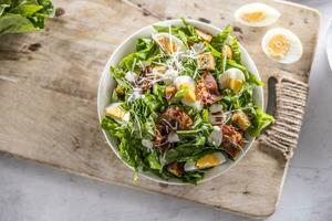 Caesar salade bereid van romaine sla, gebakken spek, ei, brood croutons, knoflook dressing en geraspt Parmezaanse kaas kaas - top van visie. foto