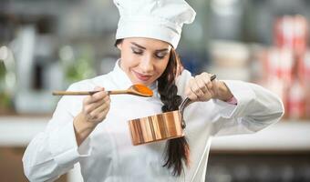 professioneel vrouw chef ruikt de saus van een houten lepel Holding een pan in de andere hand- foto