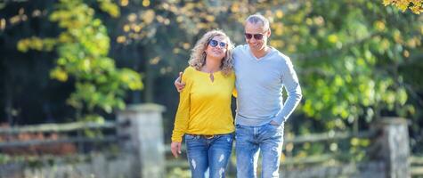 gelukkig volwassen paar in herfst park in de omhelzing wandelen Aan de gedaald esdoorn- bladeren foto