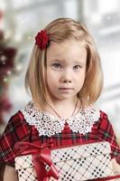 een klein meisje in een rode jurk heeft een geschenkdoos in haar handen foto