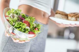 vrouw Holding bord met calorierijk cakes en salade. foto