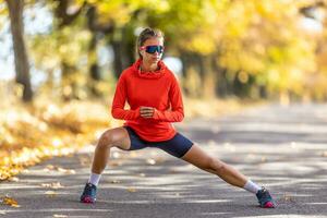 jong vrouw atleet in sportkleding is opwarming omhoog voordat rennen in de herfst park foto