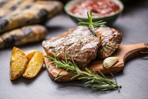 geroosterd rundvlees steak Aan houten bord met aardappelen en rozemarijn. foto