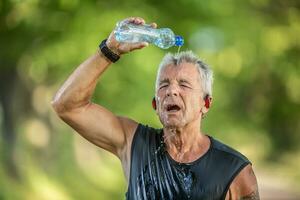 gepensioneerde mannetje loper koelt af naar beneden door gieten vers water van een fles over- zijn hoofd foto