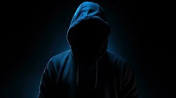 onherkenbaar figuur in donker blauw capuchon verborgen gezicht armen gekruiste eenzaam in duisternis. silhouet concept foto