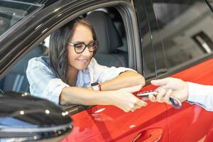 gelukkig vrouw ontvangen de sleutels van haar nieuw rood auto van de verkoper foto