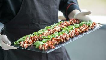 chef in hotel of restaurant Holding in haar handen leisteen bord met caprese salade foto