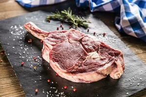 rauw rundvlees tomahawk steak met zout peper en rozemarijn Aan leisteen bord foto