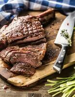 vers gegrild tomahawk steak Aan leisteen bord met zout peper rozemarijn en peterselie kruiden. gesneden stukken van sappig rundvlees steak foto