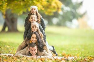 gelukkig familie piramide van ouders, tweeling meisjes en een jongen buiten omsingeld door herfst gebladerte foto