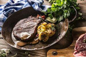 sappig rundvlees rib oog steak geroosterd aardappelen met saus gegrild groente zout peper en kruiden in wijnoogst pan foto