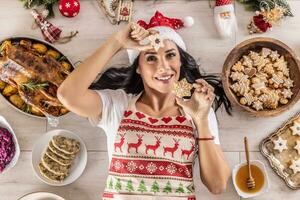 een vrolijk koken in een Kerstmis schort is aan het liegen Aan de grond Holding een linzer gebakje en een peperkoek ster omringd door traditioneel vakantie gerechten en cakes foto