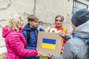 vysne nemecke, Slowakije. maart 30. 2022. vrouw met twee tieners accepteert een doos van humaitair steun voor Oekraïners in de oorlog getroffen zone foto