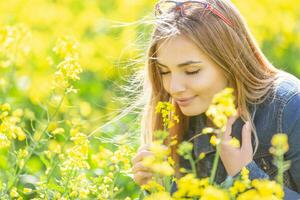mooi jong meisje ruikt geel bloemen Aan een weide met haar ogen gesloten, glimlachen foto