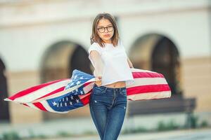 gelukkig jong Amerikaans school- meisje Holding en golvend in de stad met Verenigde Staten van Amerika vlag foto