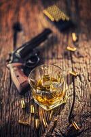 glas van whisky cognac of bourbon met revolver en kogels Aan houten tafel foto