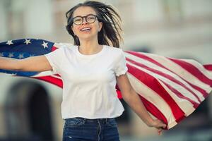 gelukkig jong Amerikaans school- meisje Holding en golvend in de stad met Verenigde Staten van Amerika vlag foto