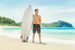 een Mens staand Aan de strand Holding een surfboard foto