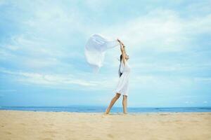 een vrouw in een wit jurk staand Aan de strand met een wit kleding foto