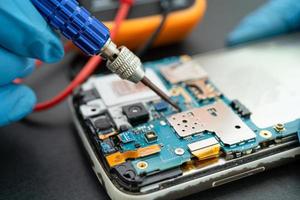 technicus die binnenkant van mobiele telefoon repareert door soldeerbout. geïntegreerde schakeling. het concept van gegevens, hardware, technologie. foto