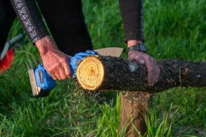 in de hand gehouden portable camping elektrisch zag Aan een accu voor snijdend brandhout en hout. detailopname, een hand- zagen een log, splinters vliegend foto