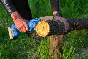 in de hand gehouden portable camping elektrisch zag Aan een accu voor snijdend brandhout en hout. detailopname, een hand- zagen een log, splinters vliegend foto