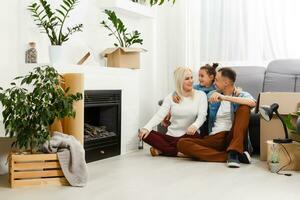 gelukkig familie zittend Aan houten vloer. vader, moeder en kind hebben pret samen. in beweging huis dag, nieuw huis en ontwerp interieur concept foto