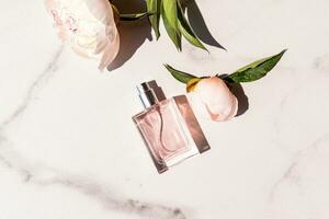 een transparant fles van vrouwen parfum met een delicaat bloemen aroma voor elke dag. top visie. marmeren wit achtergrond met leven pioenrozen. een kopiëren ruimte. foto