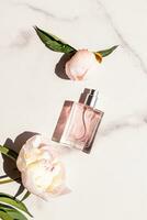 een chique fles van vrouwelijk parfum of kunstmatig verstuiven Aan een marmeren wit achtergrond met een mooi pioen en bloem knop. top visie. presentatie foto