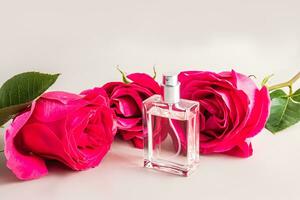 een fles van parfum gemaakt van transparant glas tegen de achtergrond van mooi bloemknoppen van rood rozen. sjabloon voor parfum en eau de toilet. foto