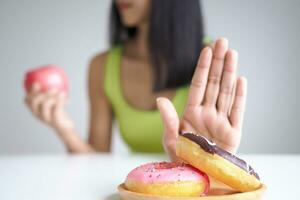 eetpatroon en op dieet zijn. schoonheid slank vrouw lichaam verwarren donut. vrouw in oefening kleren behaalt gewicht verlies doel voor gezond leven, gek over dunheid, dun taille, voedingsdeskundige. foto