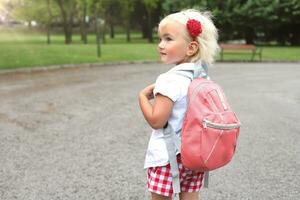 weinig blond meisje met roze rugzak in park, levensstijl gaan naar school- foto