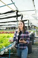 Aziatisch vrouw boer op zoek biologisch groenten en Holding tablet voor controle bestellingen of kwaliteit boerderij foto