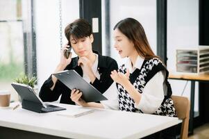 twee Aziatisch bedrijf arbeiders pratend Aan de smartphone en gebruik makend van laptop Bij de modern kantoor. foto