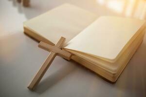 kruis vertegenwoordigt god geplaatst Aan Bijbel welke is onderwijs van god volgens naar christen vertrouwen. kruis en Bijbel waren geplaatst Aan tafel in kamer net zo ze waren bereid voor gebeden naar god door vertrouwen. foto