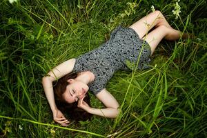 brunette vrouw aan het liegen Aan groen gras. schoonheid meisje buitenshuis genieten van natuur en ontspanning. vrij gelukkig vrouw, top visie foto