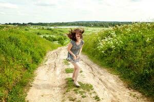 schoonheid meisje buitenshuis genieten van natuur. mooi vrouw jumping Aan zomer veld- met bloeiend wild bloemen, zon licht. vrij gelukkig vrouw. foto