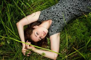brunette vrouw aan het liegen Aan groen gras. schoonheid meisje buitenshuis genieten van natuur en ontspanning. vrij gelukkig vrouw, top visie foto