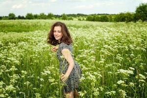 schoonheid meisje buitenshuis genieten van natuur. mooi vrouw jumping Aan zomer veld- met bloeiend wild bloemen, zon licht. vrij gelukkig vrouw. foto