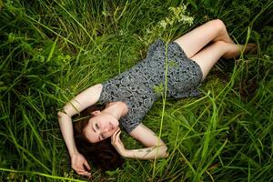 brunette vrouw aan het liegen Aan groen gras. schoonheid meisje buitenshuis genieten van natuur en ontspanning. vrij gelukkig vrouw, top visie foto