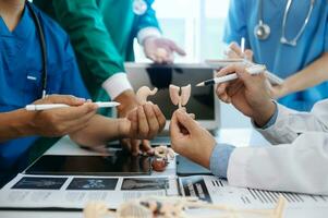 medisch team hebben een vergadering met artsen in wit laboratorium jassen en chirurgisch scrubs gezeten Bij een tafel bespreken een patiënten werken online gebruik makend van computers in de medisch industrie foto