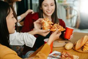 groep van vrienden maken pret Bij huis partij.zij zittend Aan bureau in leven kamer en aan het eten pizza. gelukkig foto