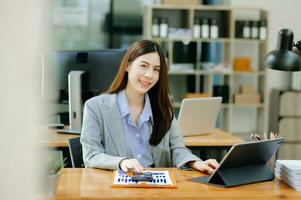 zelfverzekerd Aziatisch vrouw met een glimlach staand Holding kladblok en tablet Bij de modern kantoor. foto