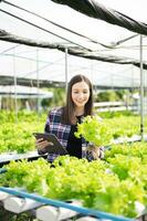 Aziatisch vrouw boer op zoek biologisch groenten en Holding tablet voor controle bestellingen of kwaliteit boerderij foto